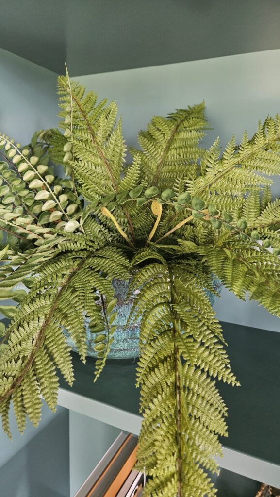 Kunstvaren met natuurgetrouw blad in een blauwgroene pot op een boekenkast